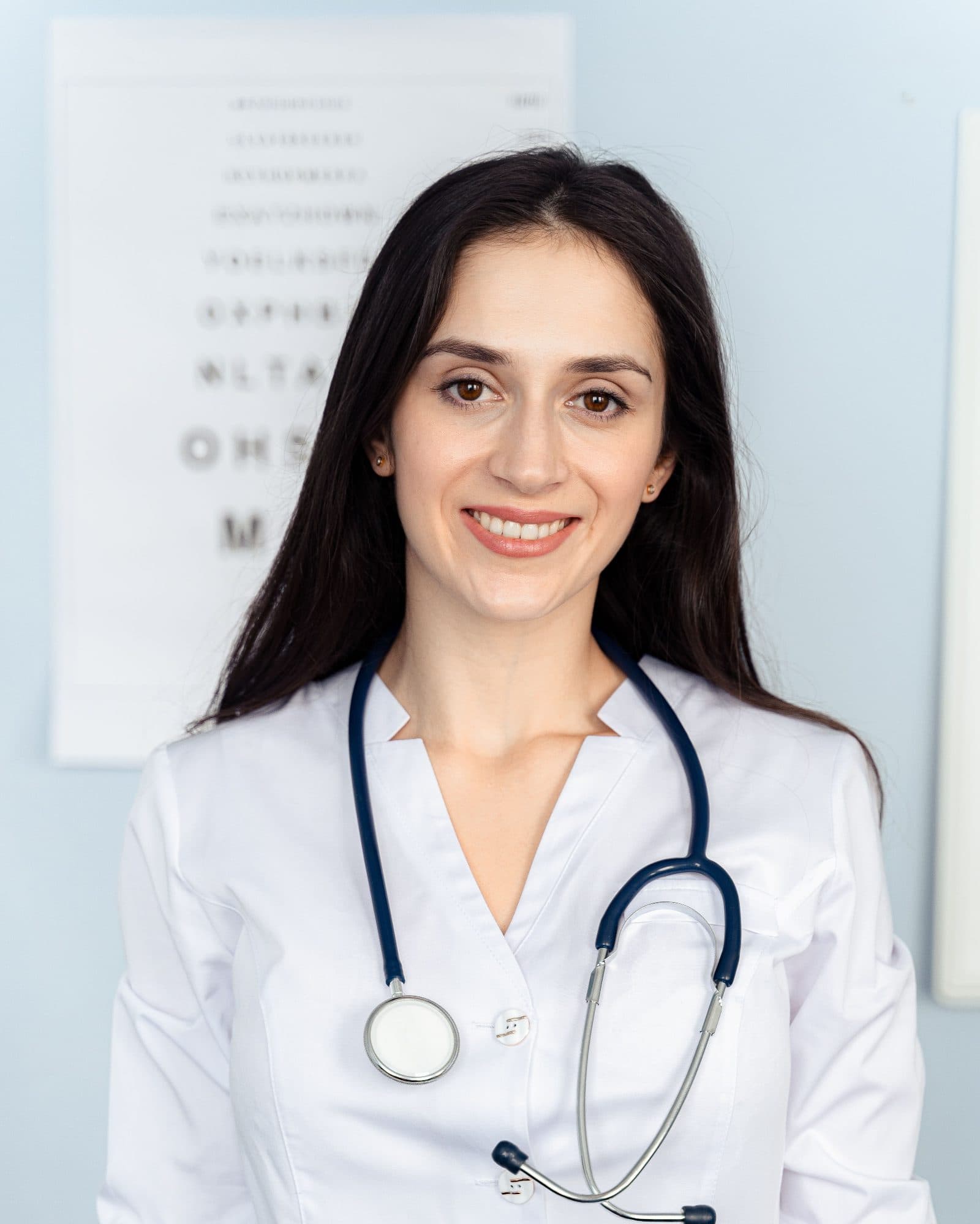 A doctor in a white coat with a stethoscope, in a consulting room.